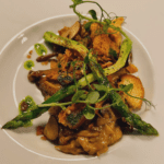 Gourmet dish featuring grilled asparagus, sautéed mushrooms, crispy croutons, and a drizzle of herb-infused oil served on a white plate.